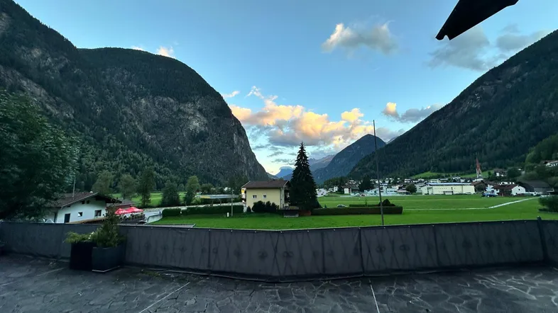 Malerischer Blick auf die umliegenden Berge und grüne Felder bei Sonnenuntergang von einer gepflasterten Fläche.