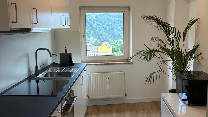 Moderne Küche mit weißen Schränken, dunkler Arbeitsplatte und Bergblick durch das Fenster.