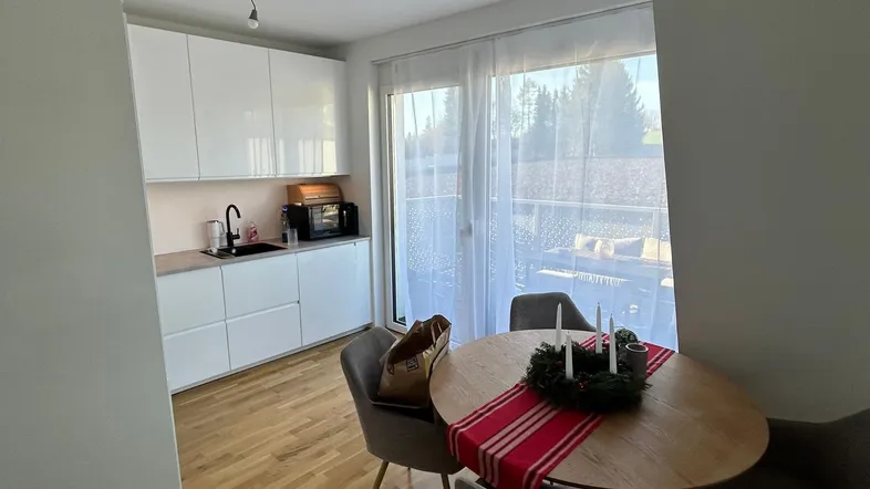 Helle Küche mit weißen Schränken, Holzboden und Essbereich, mit Zugang zu einem Außenbereich.