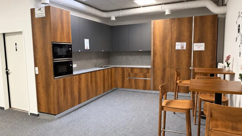 Moderne Büroküche mit Holzelementen, grauen Schränken und integrierten Geräten, ideal für Pausen.