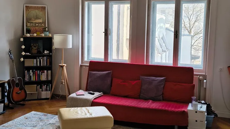 Helles Wohnzimmer mit Fischgrätparkett, rotem Sofa und großen Fenstern, die viel Licht hereinlassen.