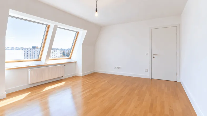 Helles Zimmer mit Holzfußboden, Dachschrägenfenstern und Blick auf die Stadt.