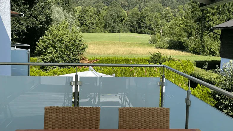 Geräumiger Balkon mit Holztisch und Korbstühlen, bietet einen weiten Blick ins Grüne und auf die Berge.