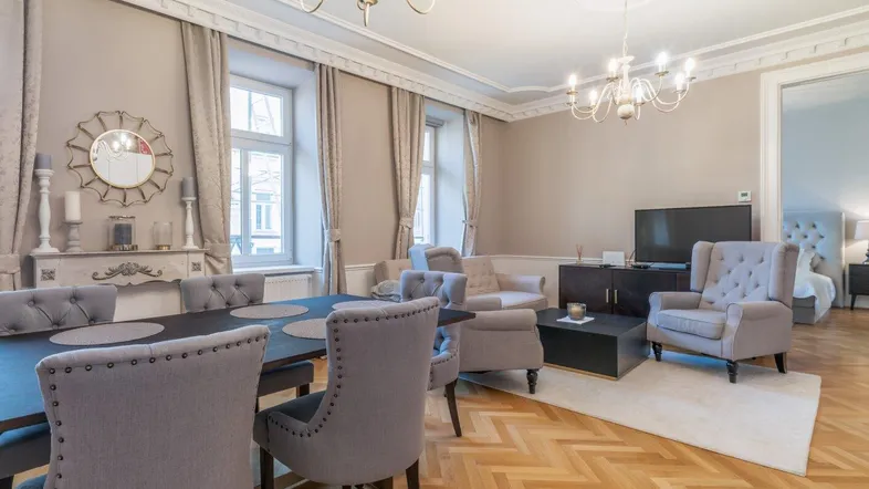 Elegantes Wohn-Esszimmer mit Fischgrätparkett, Kronleuchtern und Blick in ein Schlafzimmer.