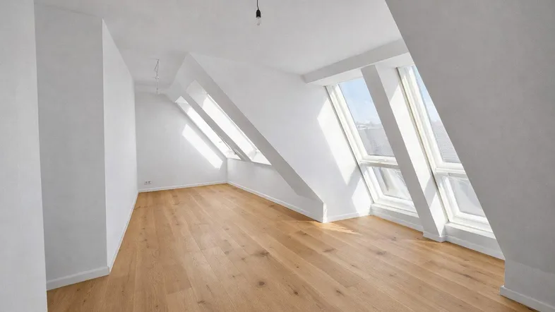 Lichtdurchflutetes Dachzimmer mit Holzboden und mehreren großen Dachfenstern.