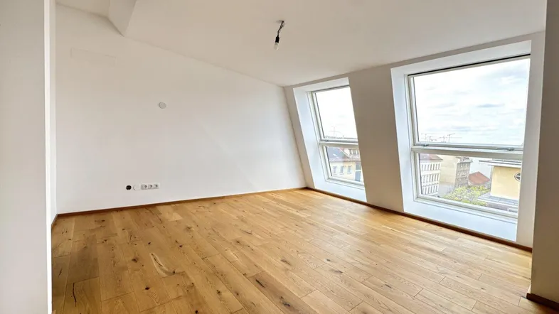 Moderner Wohnraum mit schrägen Wänden und großen Fenstern, die einen weiten Blick über die Stadt bieten.