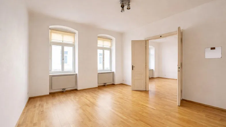 Helles, leeres Zimmer mit Parkettboden und zwei Fenstern, bereit zur individuellen Gestaltung.
