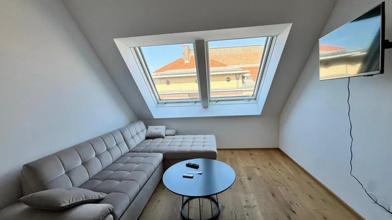 Gemütlicher Wohnbereich im Dachgeschoss mit großem Ecksofa und viel Tageslicht durch Dachfenster.