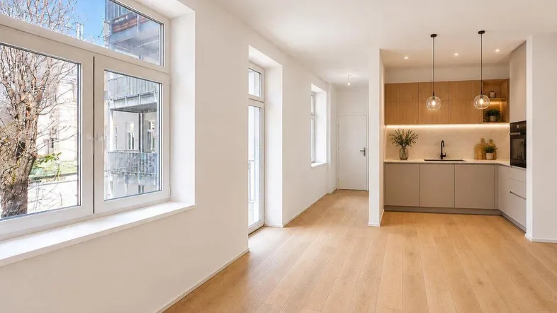 Helles, offenes Wohnzimmer mit Holzboden und integrierter moderner Küche, ideal für geselliges Beisammensein.
