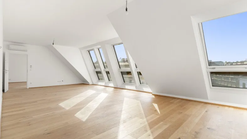 Helles Zimmer im Dachgeschoss mit Holzboden und mehreren Dachfenstern, das viel Tageslicht hereinlässt.