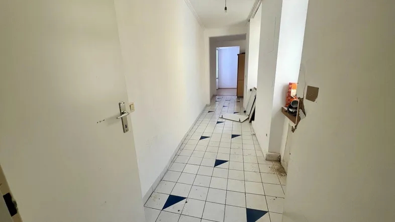 Langer Flur mit weißen Fliesen und blauen Dreiecksmustern, der zu weiteren Räumen führt.