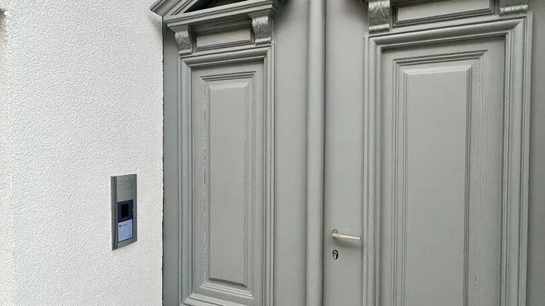 Eingangsbereich mit einer aufwendig verzierten grauen Doppeltür und moderner Gegensprechanlage.