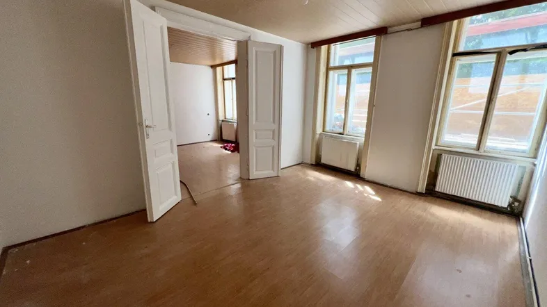Geräumiges, unmöbliertes Wohnzimmer mit Holzdecken, Parkettboden und großen Fenstern, bereit zur Renovierung.