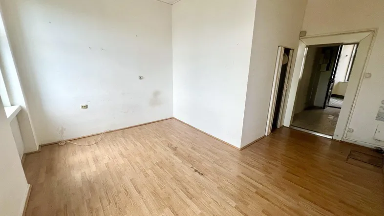 Leeres Zimmer mit Holzboden und weißen Wänden, bereit zur Renovierung und Gestaltung.