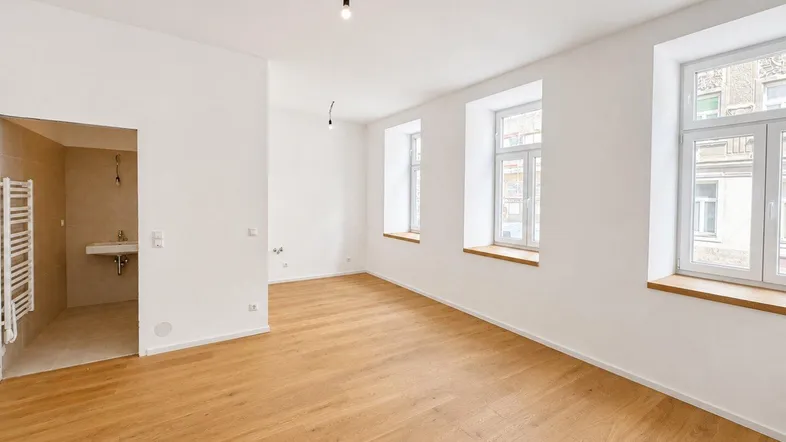 Heller, leerer Raum mit hochwertigem Parkettboden, hohen Decken und Blick auf die Stadt.