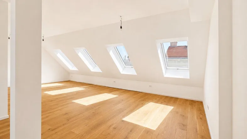 Helles Dachgeschosszimmer mit Holzboden und mehreren Dachfenstern, das viel Tageslicht hereinlässt.