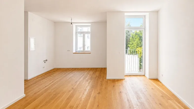 Helles, leeres Zimmer mit Holzboden und Zugang zu einem französischen Balkon.