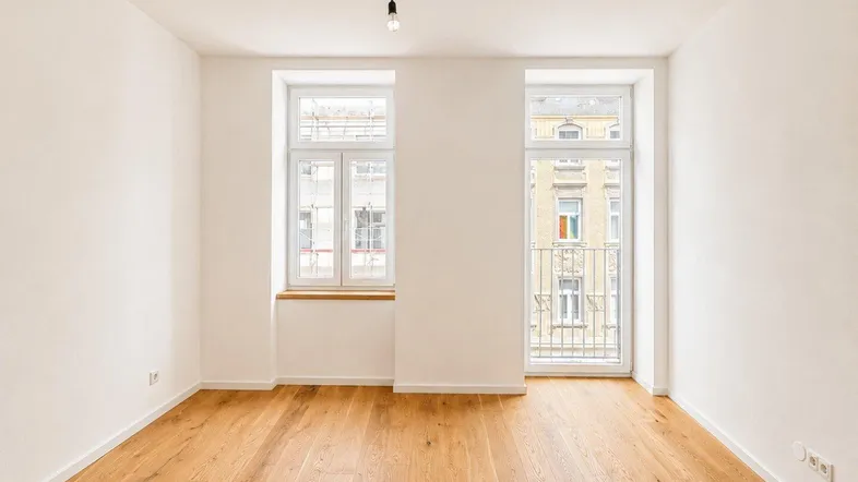 Helles Zimmer mit neuem Parkettboden, weißen Wänden und Zugang zu einem französischen Balkon.