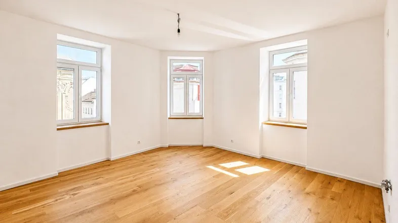 Helles Zimmer mit neuem Parkettboden und mehreren Fenstern, das viel Tageslicht hereinlässt.