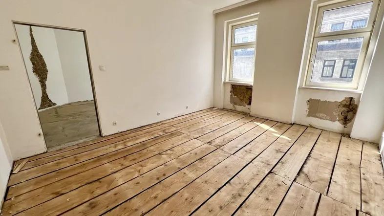 Leerer Raum mit Holzdielenboden und zwei Fenstern, bereit für die Renovierung.