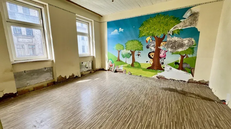 Geräumiger Raum mit farbenfroher Wandmalerei und Laminatboden, bereit für Renovierung.