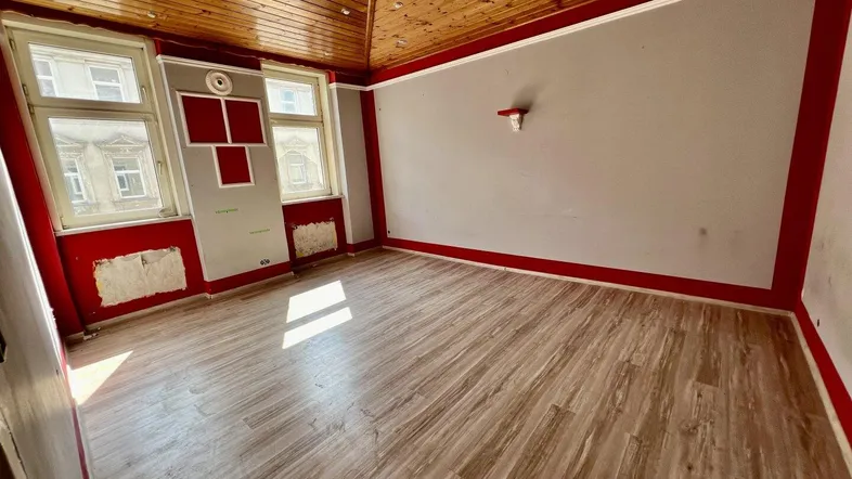 Leerer Raum mit Holzbalkendecke, Laminatboden und Fenstern, bereit zur Renovierung.