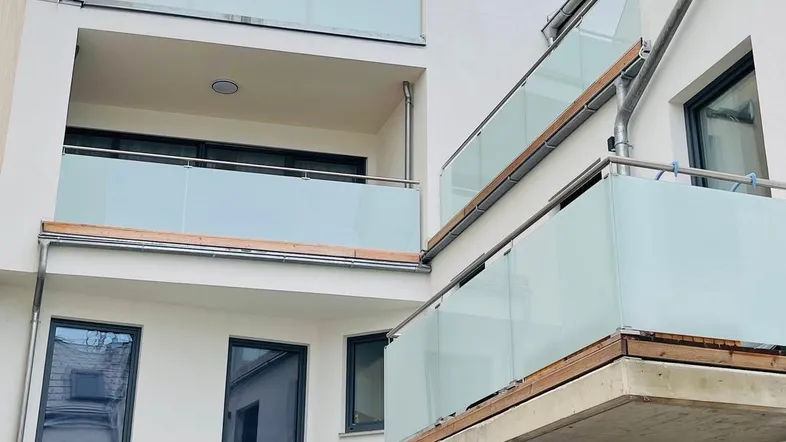 Moderne weiße Fassade eines Wohngebäudes mit mehreren Balkonen und Glasgeländern.