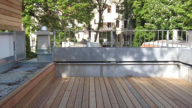 Eine neu verlegte Holzterrasse auf dem Dach mit Blick auf grüne Bäume und Gebäude.