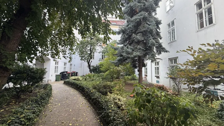 Grüner Innenhof mit gepflegten Pflanzen, Bäumen und einem geschwungenen Kiesweg zwischen den Gebäuden.