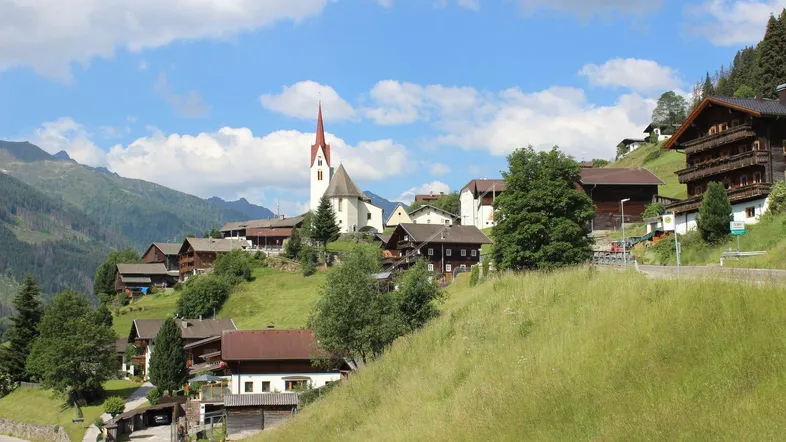 Malerisches Dorf in den Bergen mit traditionellen Häusern und einer Kirche unter blauem Himmel.
