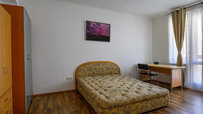 Helles Schlafzimmer mit Bett, Schreibtisch, Kleiderschränken und Zugang zu einem französischen Balkon.