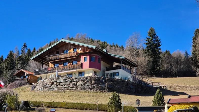 Großes Holzhaus auf einem Hügel mit mehreren Balkonen und weitem Blick.