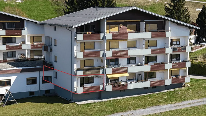 Mehrfamilienhaus mit mehreren Balkonen und Blick auf die umliegende grüne Landschaft.