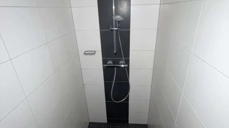 Moderne Duschkabine mit schwarz-weißen Fliesen und integrierter Duscharmatur, ideal für den täglichen Gebrauch.