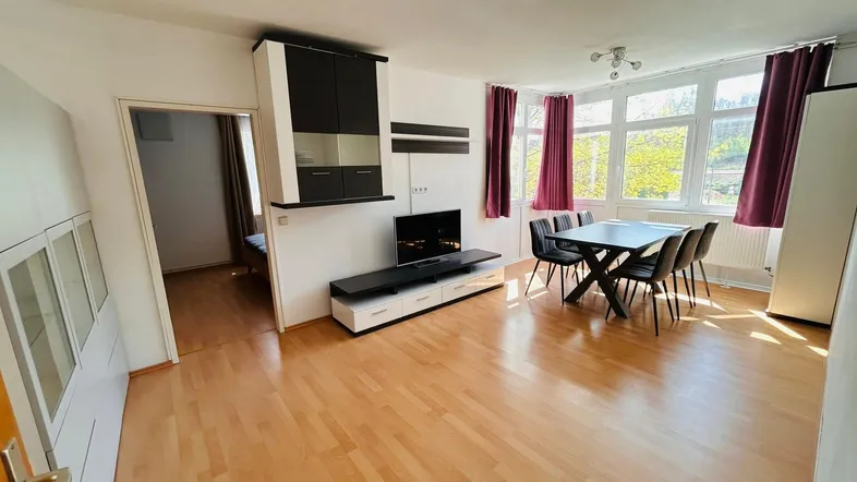 Heller Wohn-Essbereich mit Parkettboden, moderner TV-Wand und Esstisch für sechs Personen.