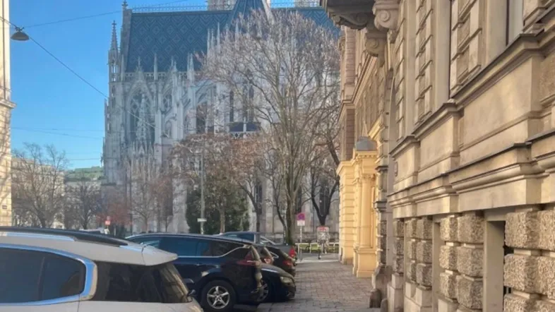 Historische Straße mit geparkten Autos und Blick auf eine imposante Kirche unter blauem Himmel.