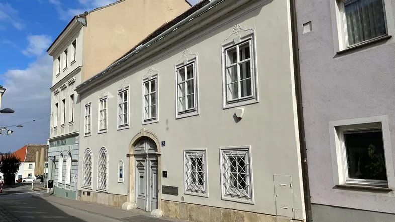Historisches Gebäude mit klassischer Fassade und verzierten Fenstern an einer ruhigen Straße.