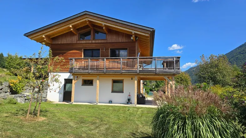 Charmantes Holzhaus mit Balkon und weitläufigem Garten unter blauem Himmel.