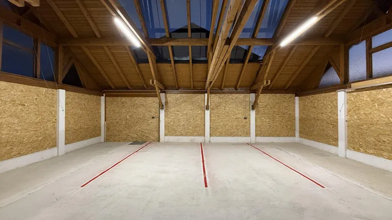 Geräumiger Innenraum mit sichtbaren Holzbalken, OSB-Wänden und Betonboden mit roten Parkmarkierungen.