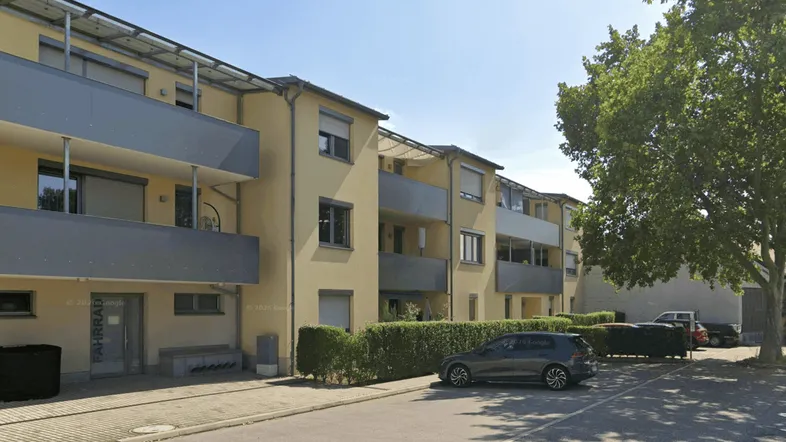 Mehrfamilienhaus mit gelber Fassade, Balkonen und Photovoltaikanlage auf dem Dach.