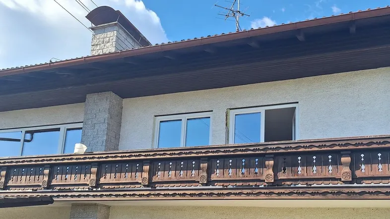 Traditioneller Balkon mit Holzelementen an der Fassade eines Wohnhauses unter blauem Himmel.
