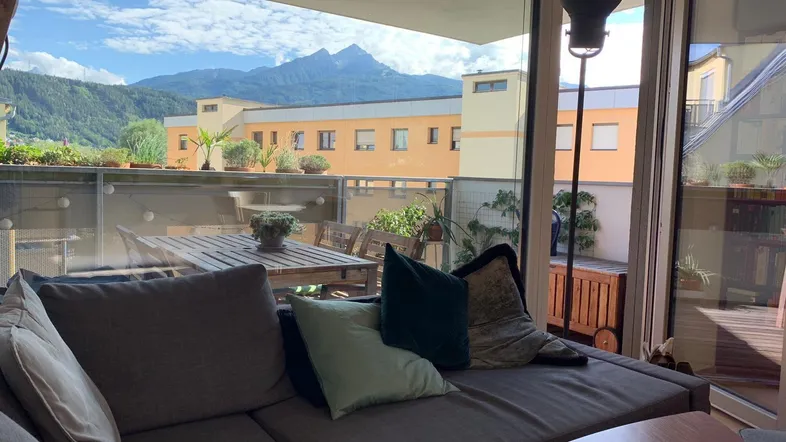 Gemütliches Wohnzimmer mit Sofa und Zugang zu einem Balkon mit Bergblick.