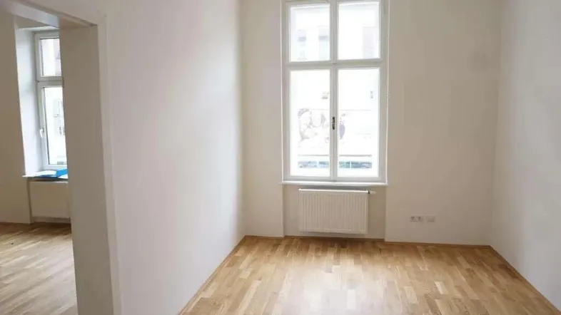 Heller Wohnraum mit Holzboden und großen Fenstern, der viel Tageslicht hereinlässt.
