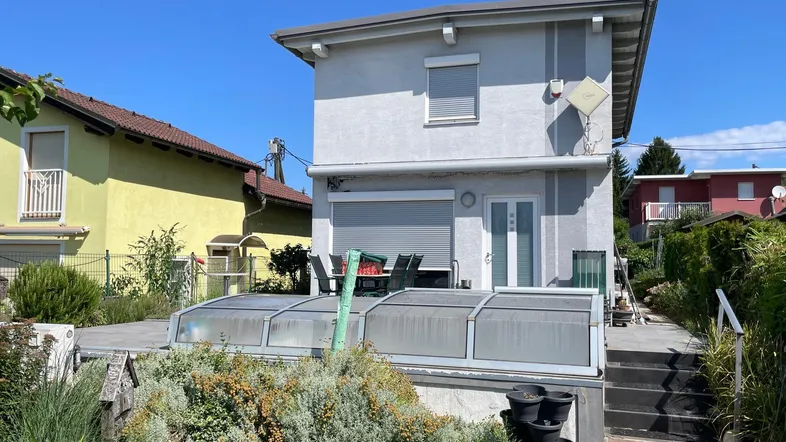 Hausfassade mit großer Terrasse, Gartenmöbeln und einem überdachten Bereich im Freien.