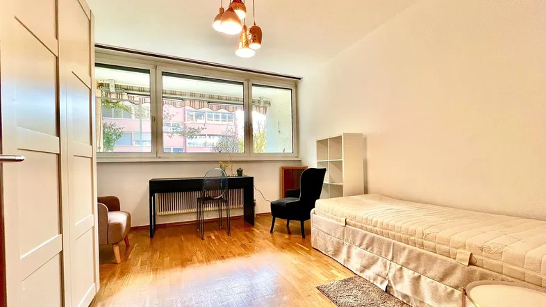 Helles Schlafzimmer mit Parkettboden, großem Fenster und modernem Deckenlicht.