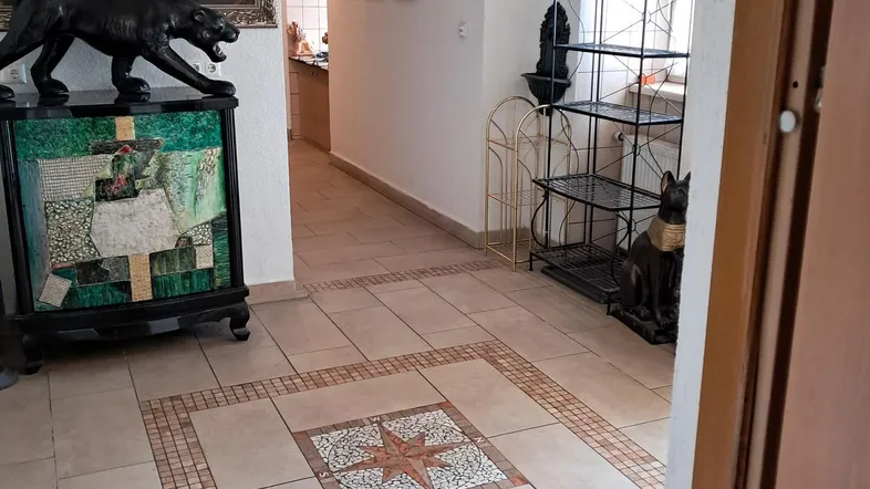Geräumiger Flur mit hellen Fliesen, dekorativem Mosaik und verschiedenen Kunstobjekten.