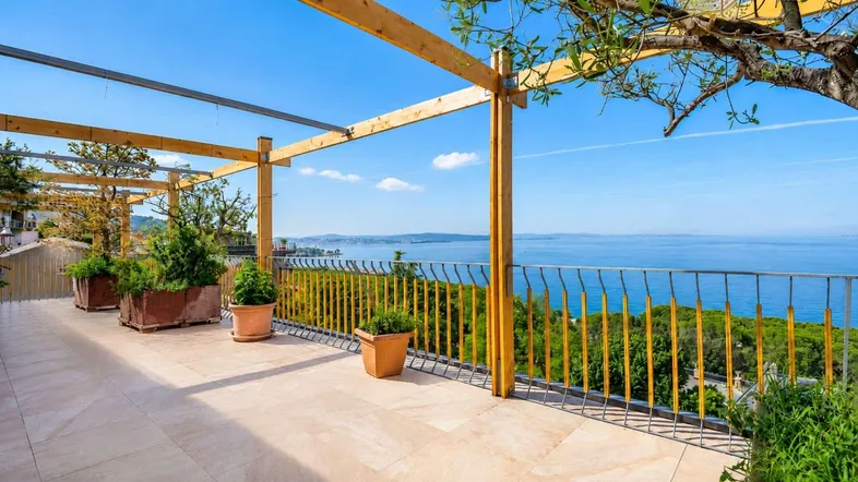 Geräumige Dachterrasse mit Fliesenboden, Holzpergola und atemberaubendem Meerblick.