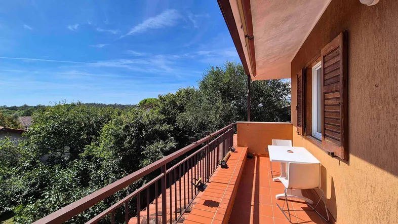 Heller Balkon mit Terrakottaboden, braunem Geländer und weitem Blick ins Grüne.