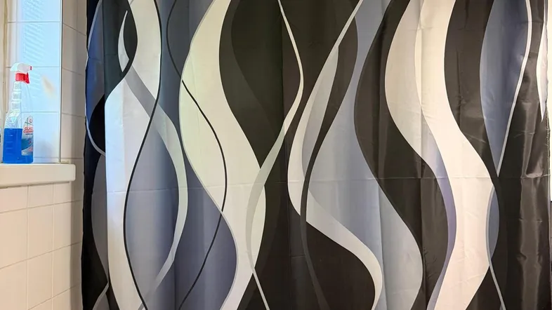 Badezimmer mit Badewanne, Duschvorhang und weißen Wandfliesen in funktionalem Zustand.
