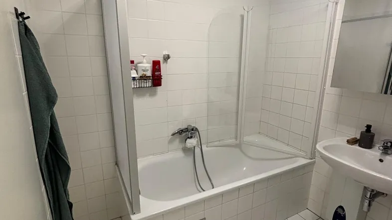 Helles Badezimmer mit Badewanne, Duschabtrennung und Fenster, ausgestattet mit weißen Fliesen.